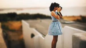 A woman photographer wearing a blue sleeveless dress takes a photograph for a free stock photography website.